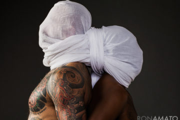 Two shirtless men, back to back, with a sheet wrapped around their heads