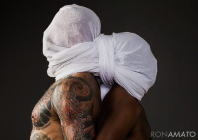 Two shirtless men, back to back, with a sheet wrapped around their heads