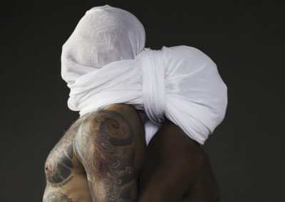 two nude men back to back with a white shroud covering their heads
