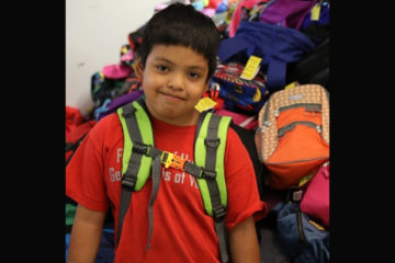 boy wearing a backpack standing in front of a pile of backpacks