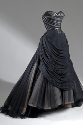 The Bustle or Swan ballgown: strapless boned bodice in black chiffon draped in folds over white satin; floor-length sweeping trained full skirt with layers of black, beige and brown net gathered into back bustle roll and forming wide polonaise or apron front swag; stiffened understructure