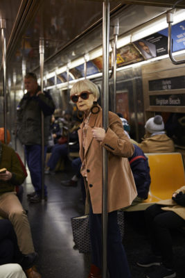 Grey haired woman with large sunglasses and tan leather jacket riding a NYC subway car