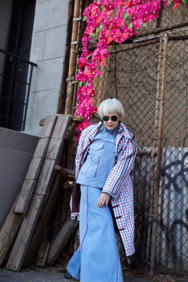 Grey haired woman in light blue skirt suit and plaid overcoat