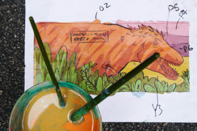 cup of water with paintbrushes shot from above over sketch of dinosaur