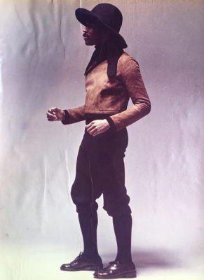 Man in Brown leather coat, black knee legth pants and wide brim felt hat.