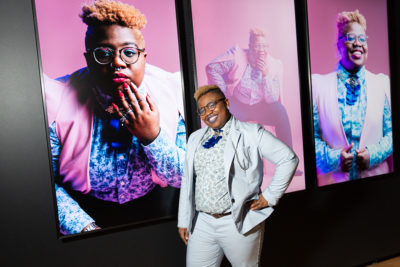 African American woman in white suit standing in front of large portrait of herself.