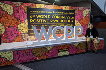 Daniel Benkendorf sitting in front of World Congress on Positive Psychology sign