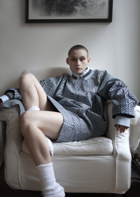 young woman with shaved head sitting on armchair in slouchy sweater dress