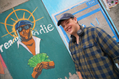 young man smiling in front of mural of rapper Christopher Wallace aka Notorious B.I.G