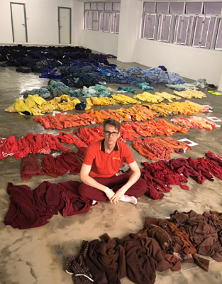 Derick Melander sitting on a floor among colorful clothing