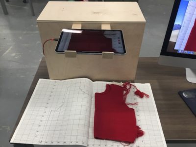 Wooden box holding iPad behind open book and red fabric scrap
