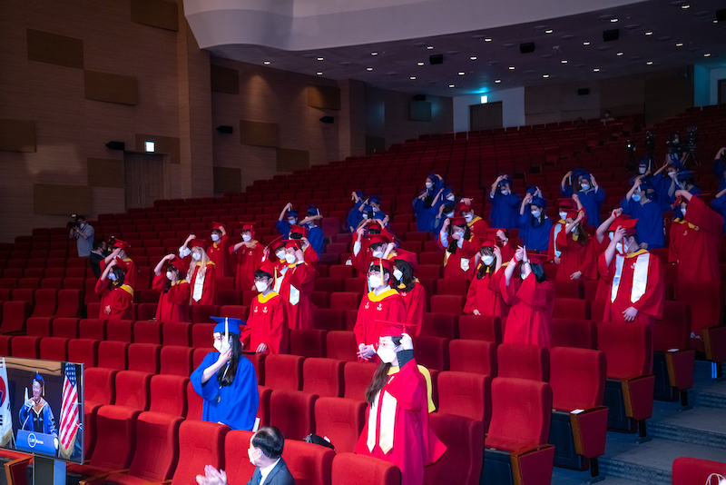 Graduates in a red theater flip their tassels