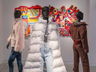 three mannequins with clothing and fabric art in the background