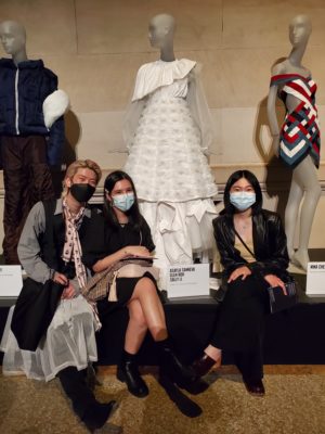 Three students sit in front of a white dress they designed at The Metropolitan Museum of Art.