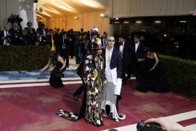 Erykah Badu in a colorful beaded robe and matching top hat with Francesco Risso, who wears sunglasses and a long white and blue garment