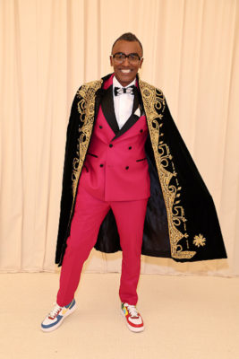 Marcus Samuelsson wearing a red tuxedo, black and gold cape, and colorful sneakers