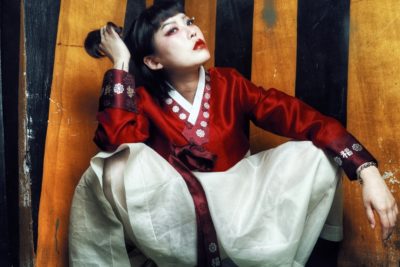 A woman squats, modeling traditional Korean clothing in a red and white color scheme