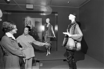 One woman is gesturing toward a garment on a mannequin in a museum exhibition.