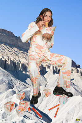 model sitting on fake glacier eating a bowl of ramen in clothing with same logo as the bowl of ramen