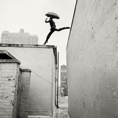 black and white photo of person jumping from one building to another