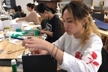 Seated female students working on interior design models at a long desk