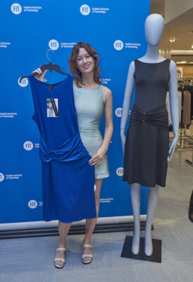 Mariah Does Hooke standing next to a mannequin in front of an FIT step and repeat in a Macy's store, holding a Macy's-fabricated version of her winning dress design