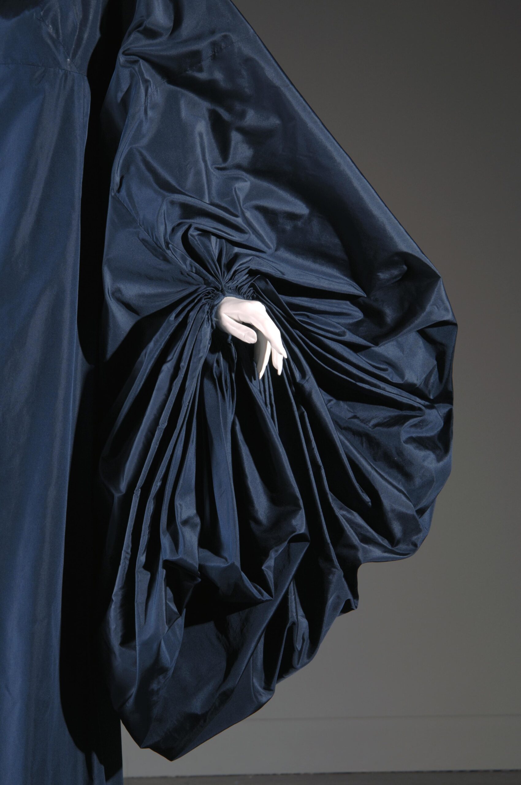 closeup of sleeve from a long evening "cape dress" in navy silk tissue taffeta. The exaggerated bishop sleeves are attached to a sleeveless underbodice, for full-length draped cape effect over slightly A-line skirt.