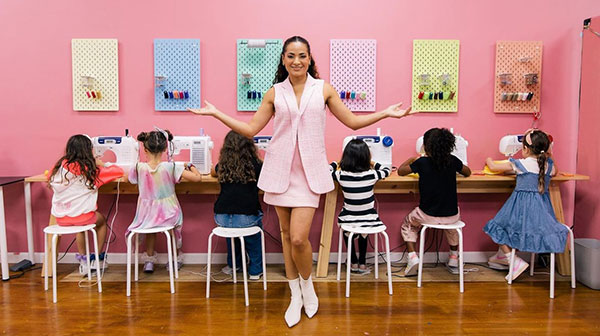 Layana Aguilar standing in front of a group of children seated at sewing machines in a pink room