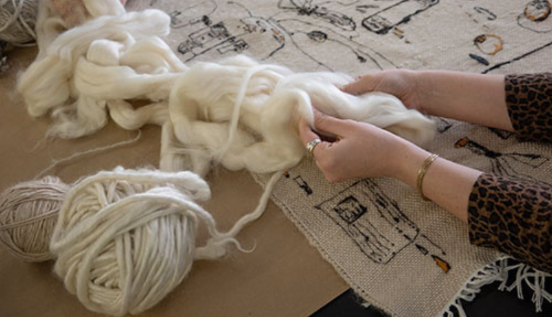 hands pulling wool into yarn at a desk