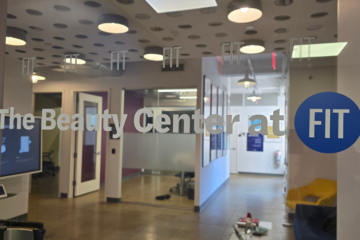 looking through glass door at The Beauty Center at FIT into the lobby with a chair, lights, reception