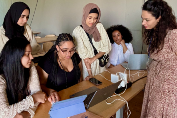 students surround an instructor at a desk