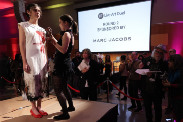 student paints canvas on model on a stage in front of audience