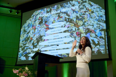 Liz Alessi on stage gesturing to a chart onscreen behind her