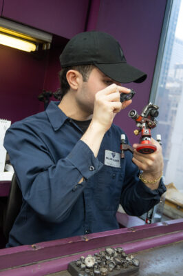 Young man in baseball cap looks at a diamond through a small magnifying lens