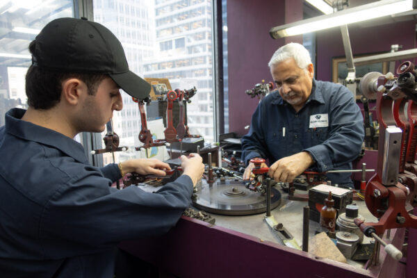 A young man in a baseball cap and an older man working at a diamond cutting bench