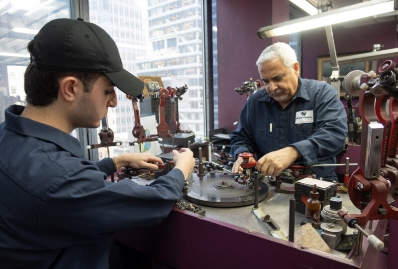 A young man in a baseball cap and an older man working at a diamond cutting bench