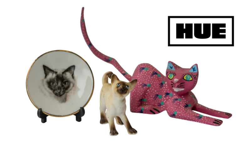 a decorative plate with a Siamese cat on it; a Siamese cat figurine; a pink handpainted cat figurine; Hue logo