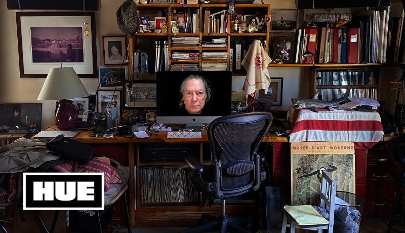 Denton Tillman's home office with a desk, bookshelves, and desktop computer with a photo of his face looking straight out from the computer screen; Hue logo 