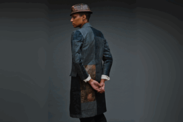 Model wearing patchwork topcoat and brown fedora-style hat.