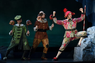 Three men wearing 18th century clown costumes in a production of an opera.