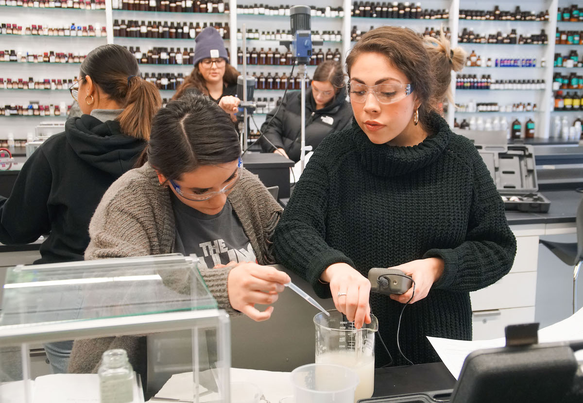 several students perform experiments in the FIT fragrance lab, two in the foreground are working with a beaker filled with white fluid
