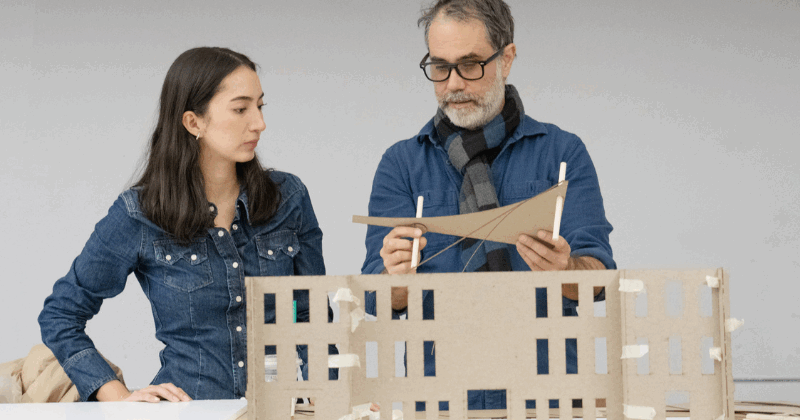 a student and teacher stand in front of a miniature exhibition model