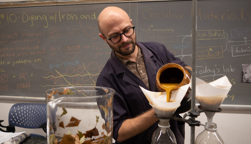 Julian Silverman in his classroom pouring a yellow substance into a beaker