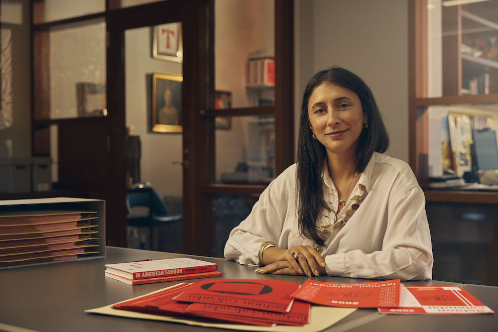 Natalie Nudell sits at a desk with copies of the Fashion Calendar in front of her. 