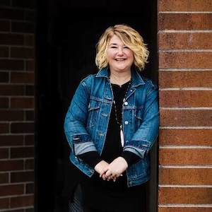 Cheerful woman in jean jacket leaning against brick wall