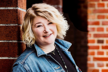 Headshot of woman in jean jacket against brick wall