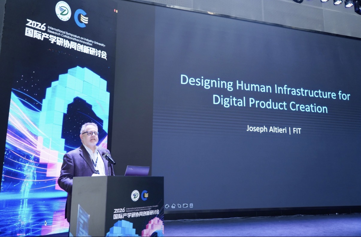 Joseph Altieri standing at a podium at a conference with large screens behind him