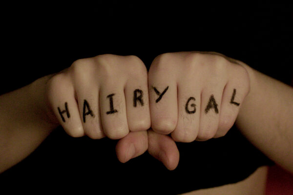 Two fists with the word HAIRYGAL written in marker on the fingers