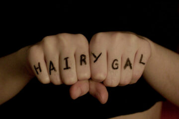 Two fists with the word HAIRYGAL written in marker on the fingers