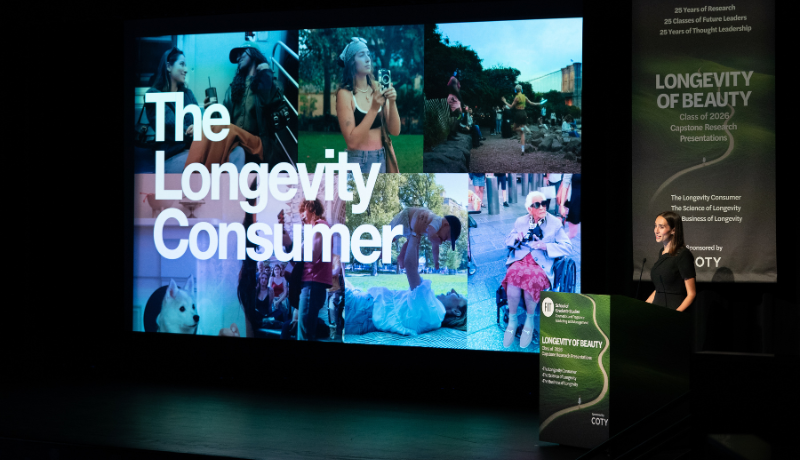 student at a lectern giving a presentation with a large screen to her right with a montage of images of people doing daily things with the text 'The Longevity Consumer'